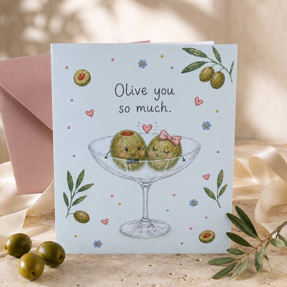 “Olive you so much.” martini-glass card standing beside a pink envelope, olives and olive branches.