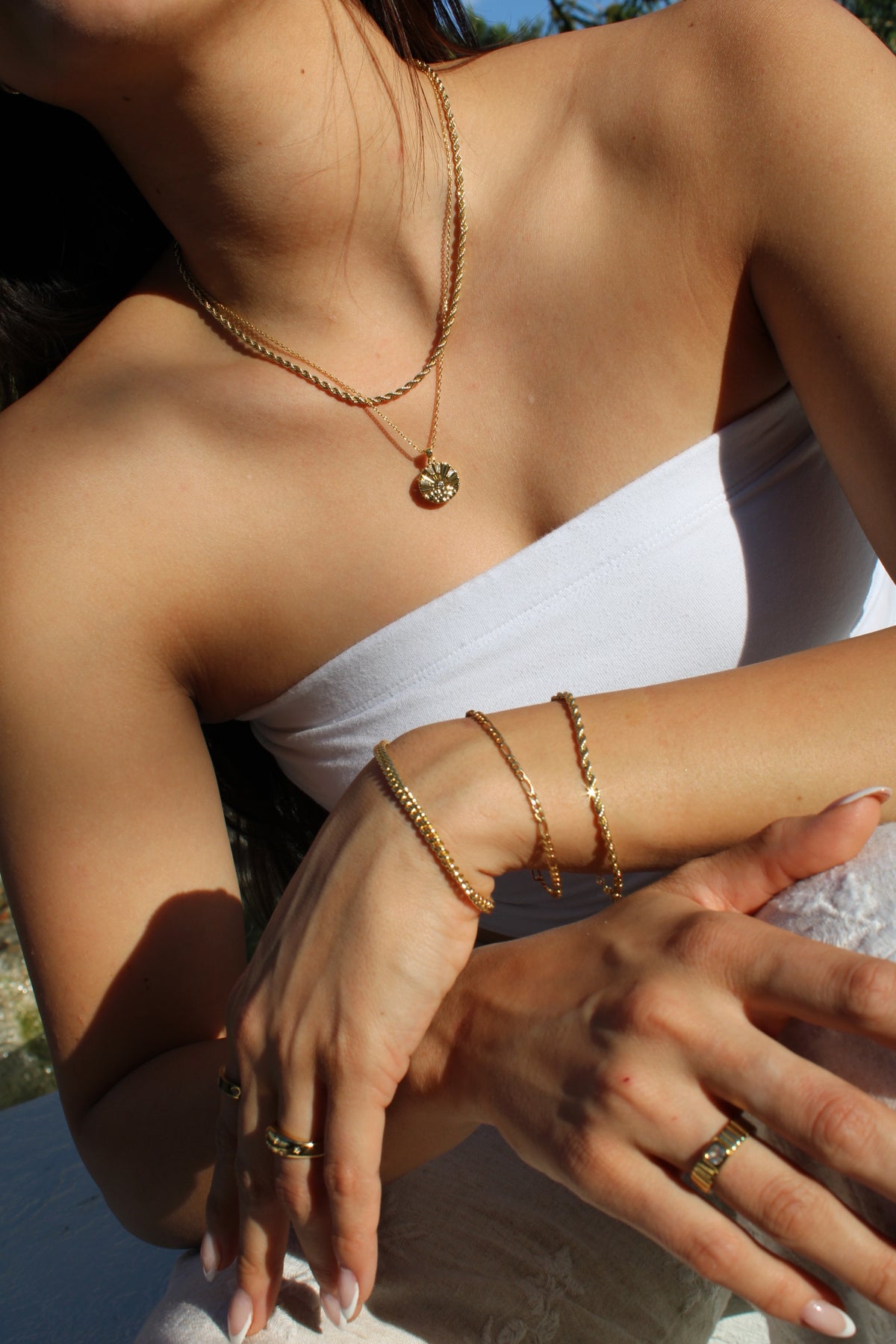 Close-up of the Sunrise Coin Necklace layered with a rope chain and styled with gold-tone bracelets and rings.