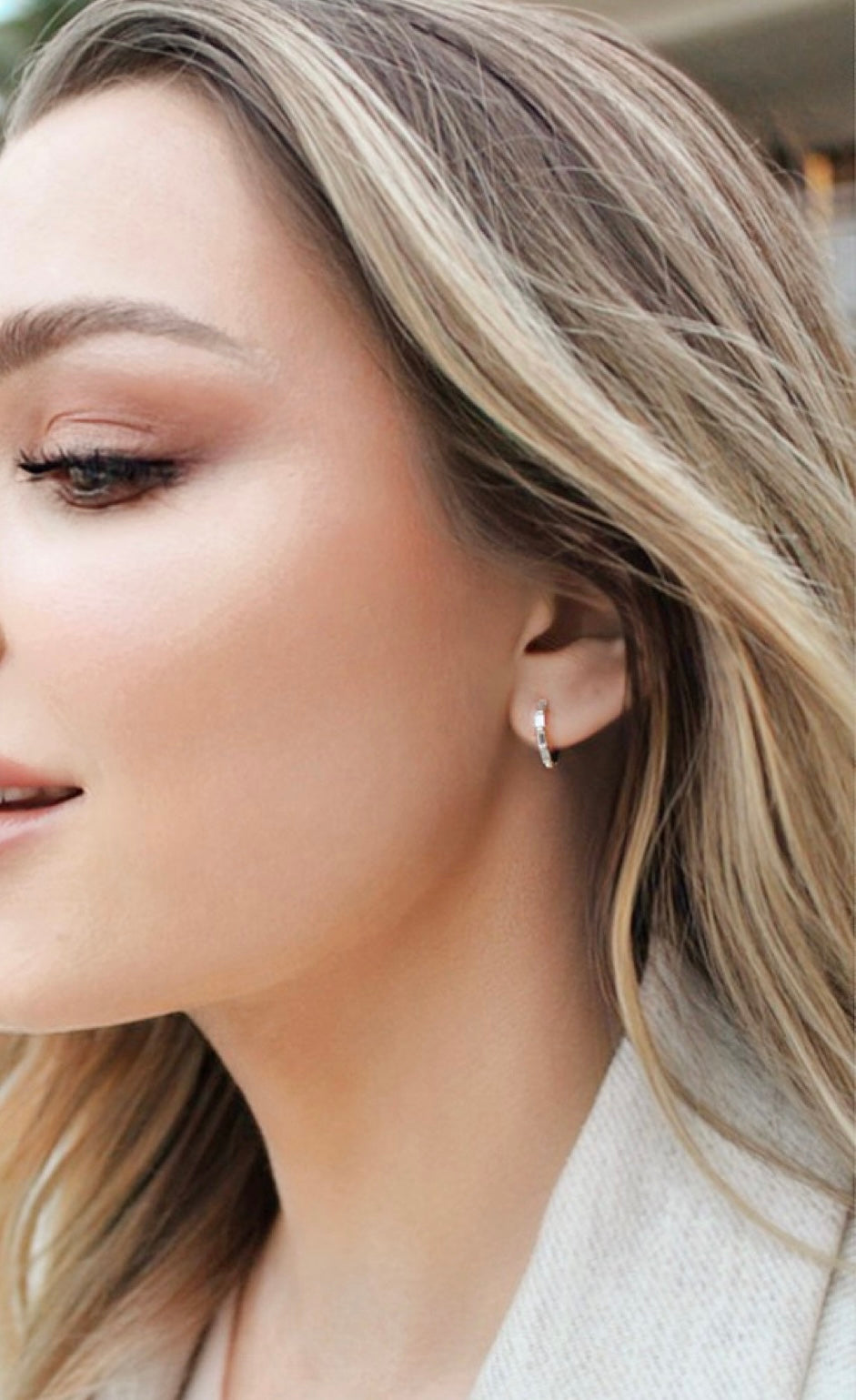 Close-up of an Angie huggie earring worn on the ear, showing the rectangular clear stones and snug hoop fit.