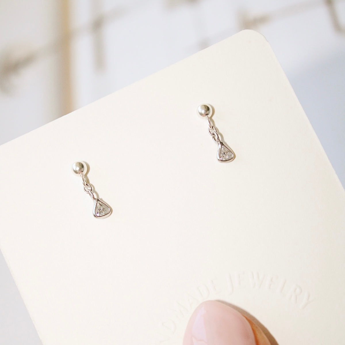 Hand-held display card with Lexy sterling silver earrings, showing the small triangular cubic zirconia drops in natural light.
