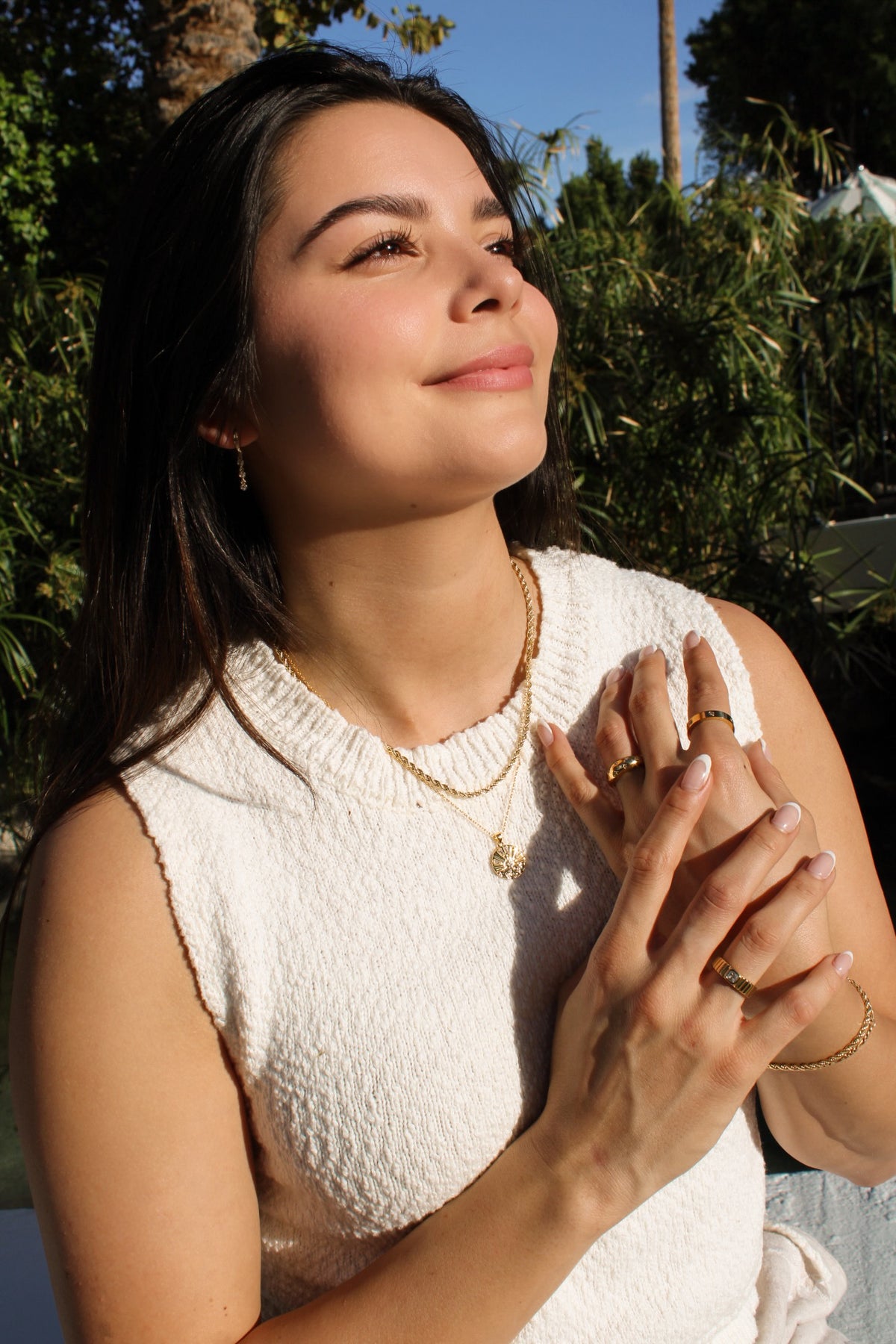 Model wearing the Star Dust ring with other gold-tone rings, layered necklaces and a bracelet outdoors.