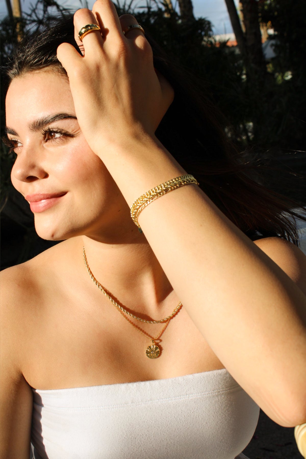 Model wearing the Sunrise Coin Necklace with a shorter gold-tone chain and stacked bracelets outdoors.