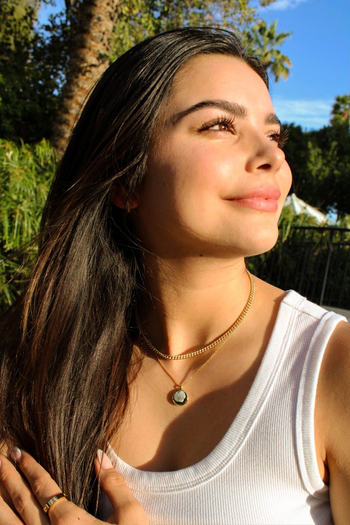 Model wearing the Taylor curb-chain necklace layered above a round pendant with a white tank top outdoors.