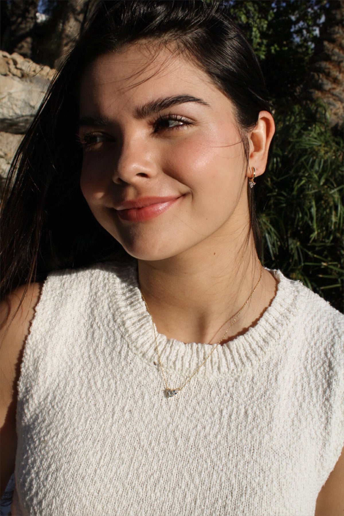 A model wears the delicate Double Stone Necklace with a sleeveless white knit top outdoors.