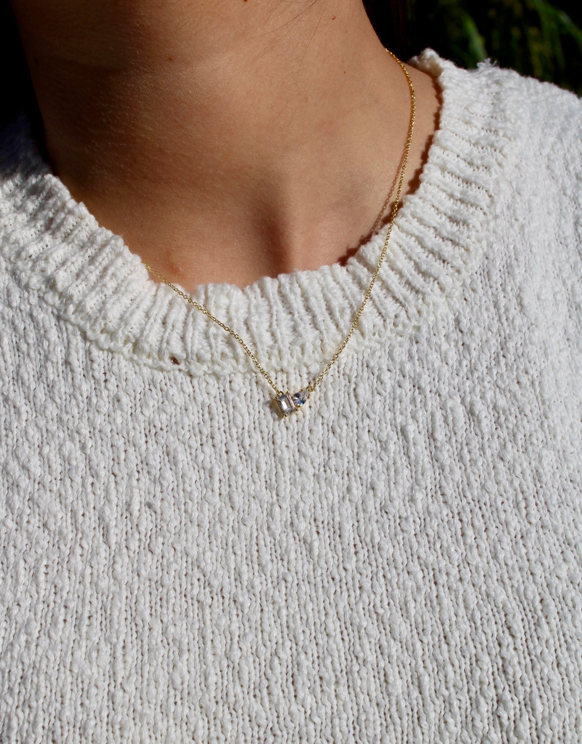 Close-up of the Double Stone Necklace worn over a white knit top, showing the two clear stones on its fine chain.