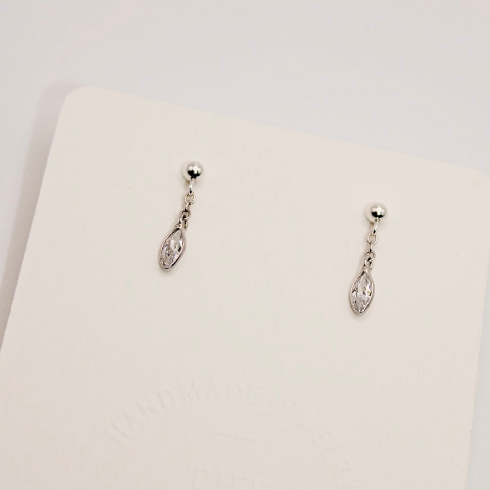 Dana sterling silver earrings with small ball studs and dangling marquise-shaped clear stones on a cream display card.