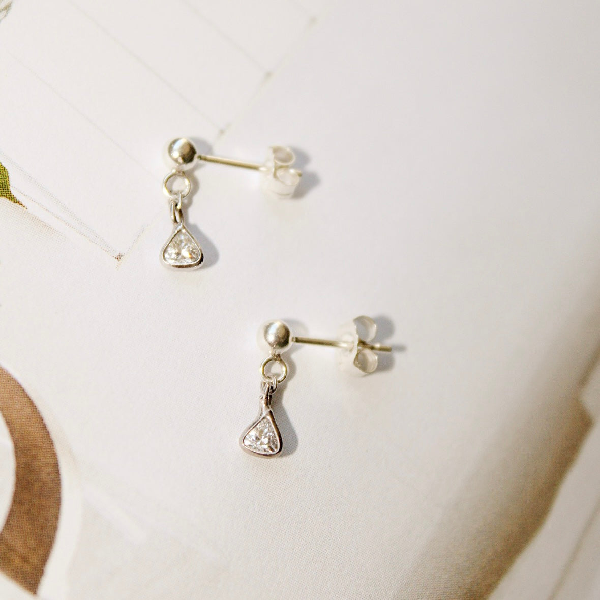 Lexy sterling silver earrings with round studs and small triangular cubic zirconia drops, laid flat with posts and backs visible.